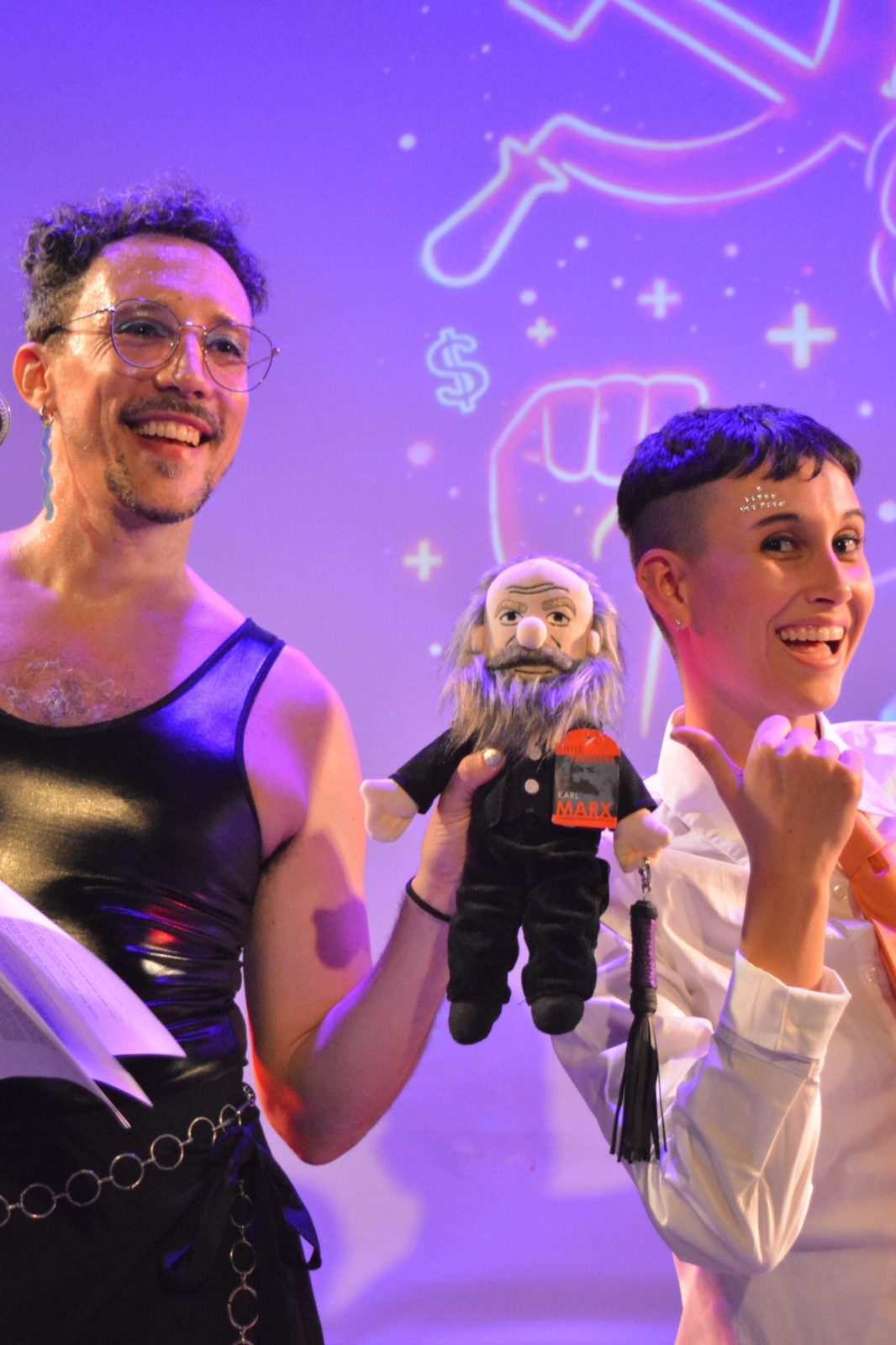 Nicol López y Lilo sonriendo en el escenario, con un muñeco de Karl Marx